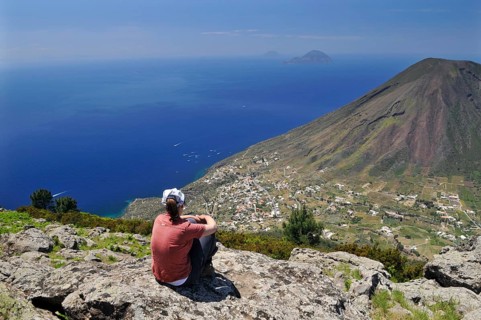 Woman sitting on a rock looking towards Filicudi and Alicudi, Salina, Aeolian or Lipari Islands,