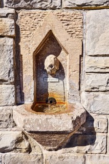 Wall fountain, public drinking water dispenser, sculpture of a fish, sandstone wall, sunny,