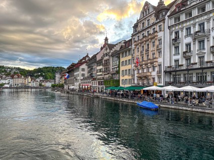 Row of historic buildings with cafés along the Reuss under a cloudy sky, Lucerne, Switzerland