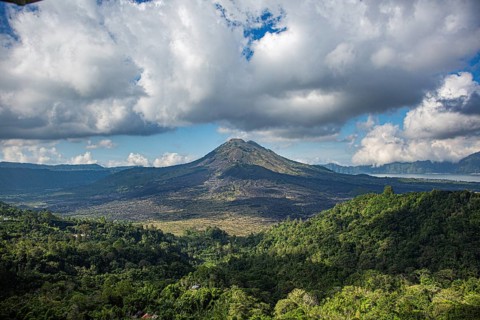 A majestic volcano rises above a lush wooded landscape under dramatic clouds, view of the caldera