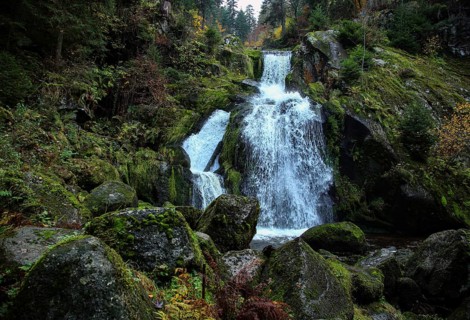 Impressive waterfall with moss-covered rocks and surrounded by dense forest, upper part of the