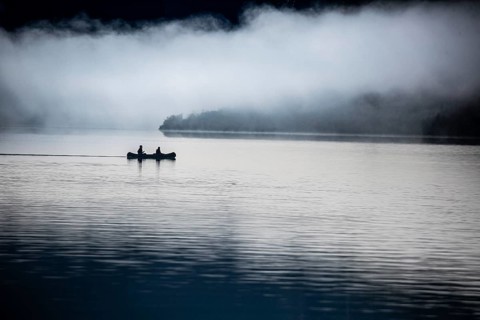 Two people in a boat on a calm lake surrounded by fog, two kayakers paddle in the morning in fog on