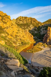 A small river flowing through the mountains into the sea, past a sandy beach in Costa Paradiso on a