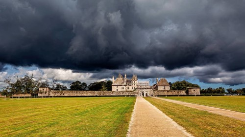 A castle under a looming sky with stormy clouds and an open lawn, The Château de Kerjean Castle in