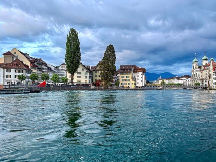 City view with church, trees and mountains in the background under a cloudy sky, Lucerne,