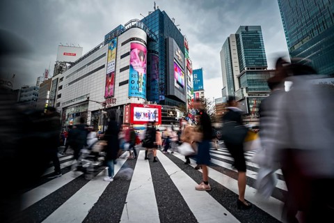 Crowd crossing zebra crossing on a large intersection, motion blur, back modern houses with