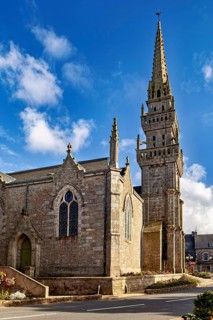 Historic Gothic church with high tower and decorated details under a clear blue sky, Saint-Edern
