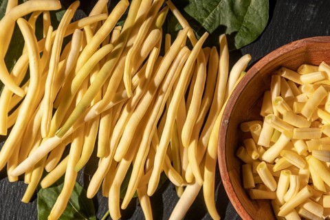 Sliced yellow beans in a bowl next to other beans and leaves