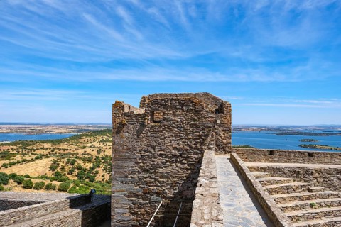 Old stone wall with tower and wide views of countryside and water under blue sky, Monsaraz, Évora,