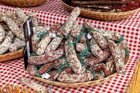 A basket of curled salamis on a red and white checkered table at a market, market stalls in