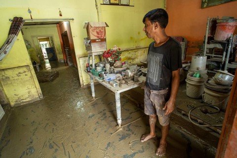 Resident walks around inside his mud-filled and flood-damaged home after floodwaters receded on