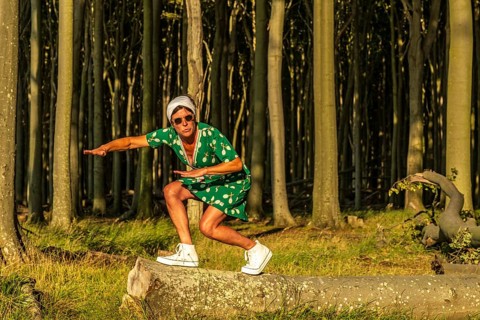 A woman (54) wearing a green tennis dress and white trainers is surfing on a tree, Ghost Forest,