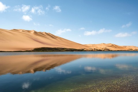 Sand dunes are reflected in the lagoon at Sandwich Harbour, Namib Naukluft Park, Namib Desert,