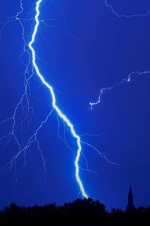 Forked lightning bolt, cloud-to-ground lightning strike during thunderstorm in blue night sky over
