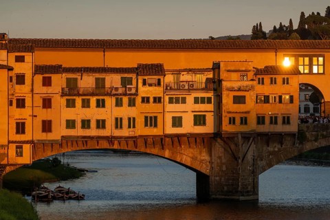 Warm evening light falls on the historic Ponte Vecchio segmental arch bridge across the Arno River