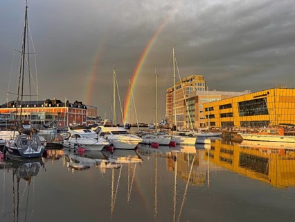 Rainbow over a marina with numerous boats and modern buildings in the background, University,