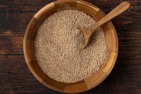 Quinoa in a wooden bowl with a spoon on a dark wooden table