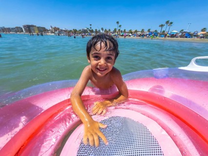 Adorable young boy smiling at the camera while playing in the ocean with an inflatable swimming