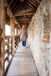Woman walking along a narrow wooden tunnel flanked by rustic stone walls, Isny, Allgäu, Bavaria,