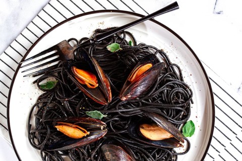 Black spaghetti with mussels, on a white plate with a fork, on a striped napkin, marble background,