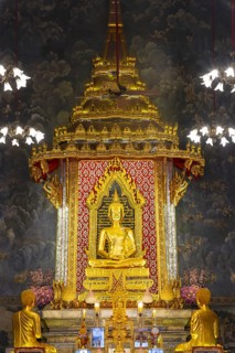 Golden meditating Buddha surrounded by wall paintings with Buddhist teachings and representations