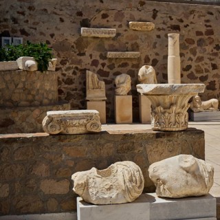 Ancient sculptures and remains of columns in front of a stone wall, Plaka Archaeological Museum,