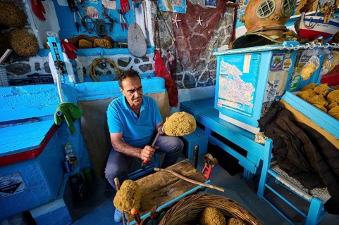 A man works on a sponge in a blue workshop with traditional tools, sponge moufactory, Nikolas