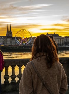 Woman standing on a bridge admiring the illuminated ferris wheel and cathedral in bayonne, france,