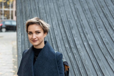 Short-haired blonde in coat smiles standing in the city. A woman with short light hair stands