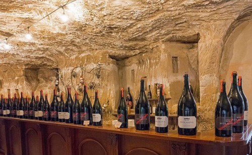 Large wine bottles stand on a long shelf in an illuminated cellar environment, sales room, Milestii