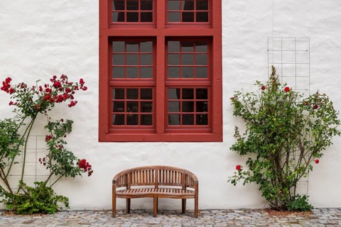 Wooden bench in front of a white wall with red windows and roses, harmonious place, Bad Iburg,
