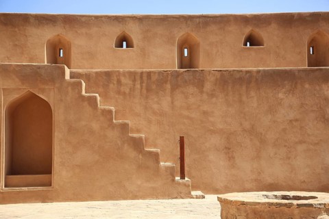 Beige sandstone wall with stairs and narrow windows in traditional architecture, courtyard, Nizwa