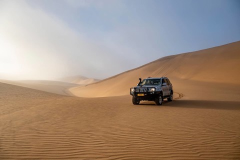 Off-road vehicle between high dunes, sea of dunes, Sandwich Harbour, impressive desert landscape,