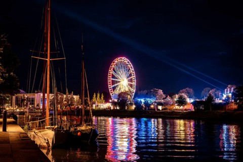 Ferris wheel in neon light, evening at a funfair, seen from the waterfront, Lübeck, Germany