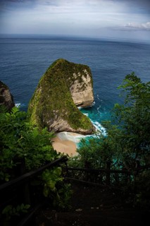 An impressive coastal cliff with lush vegetation and calm, turquoise waters, looking down from