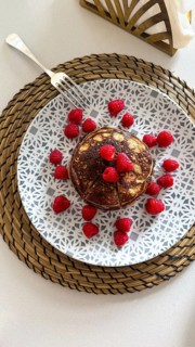 Stack of homemade pancakes topped with vibrant red raspberries, presented on a decorative plate