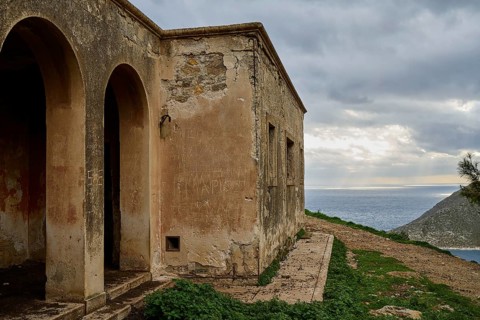 Dilapidated building overlooking the sea, characterized by arches, under a cloudy sky, Lost Place,