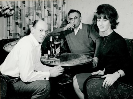 Three people sitting at a table with drinks in a cosy indoor scene from the 1960s, Herbert Jacobi