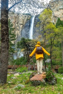 Hiker in yellow rain jacket and backpack standing on a rock, enjoying the powerful flow of