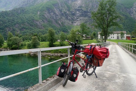 Red bike standing on a bridge over a clear river in the midst of a mountainous landscape,