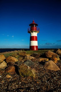 A red and white lighthouse stands under a clear blue sky on a rocky beach, Grisetaodde lighthouse,