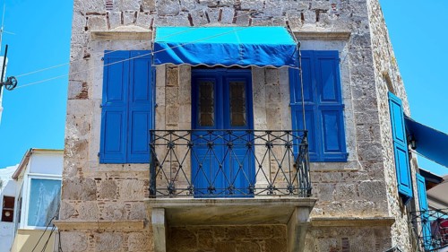Rustic stone building with blue shutters and balcony in a Mediterranean setting, Pothia, main town,