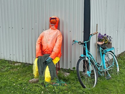 A doll dressed as a fisherman sits next to a vintage bicycle at a hut in a meadow, humor, Senja,