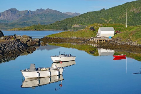 White boats are lying on a quiet lake with mountain reflections under a clear sky, Hamn, Senja,