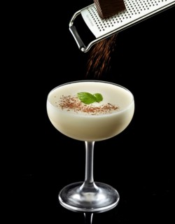 Light cocktail on a black background, grated chocolate and basil leaves as a garnish, studio shot