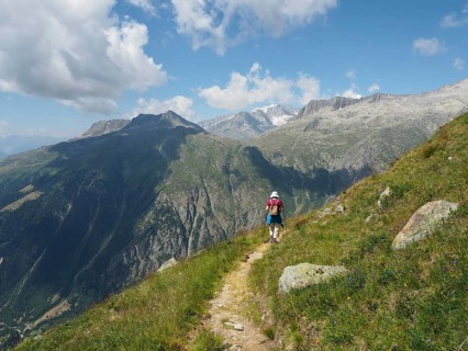 Female hiker on a rocky path with wide mountain views and blue sky with clouds, Bellwald, Goms,