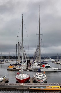 Two sailboats on the dock, surrounded by other boats in the harbor under a cloudy sky, marina with
