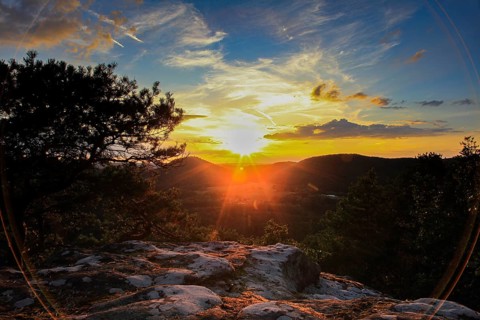 Sunset over wooded hills with clouds in the sky. Rocks in the foreground create a quiet, peaceful