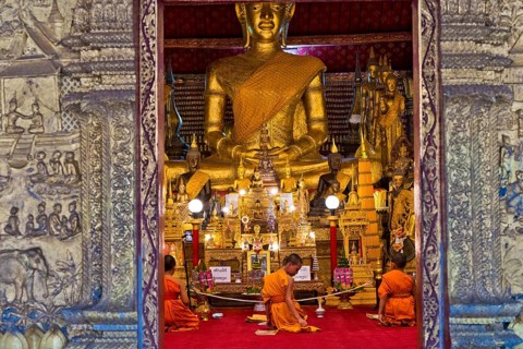 Buddhist monks and novices sit in front of a large Buddha statue in Wat May Souvannapoumaram, Luang