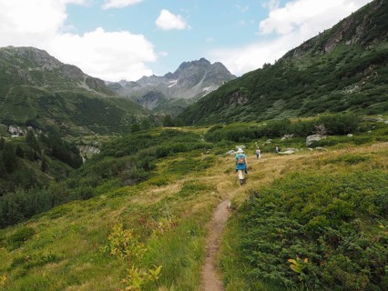 Summer mountain landscape with hiking trail, lush greenery and mountains in the background, people